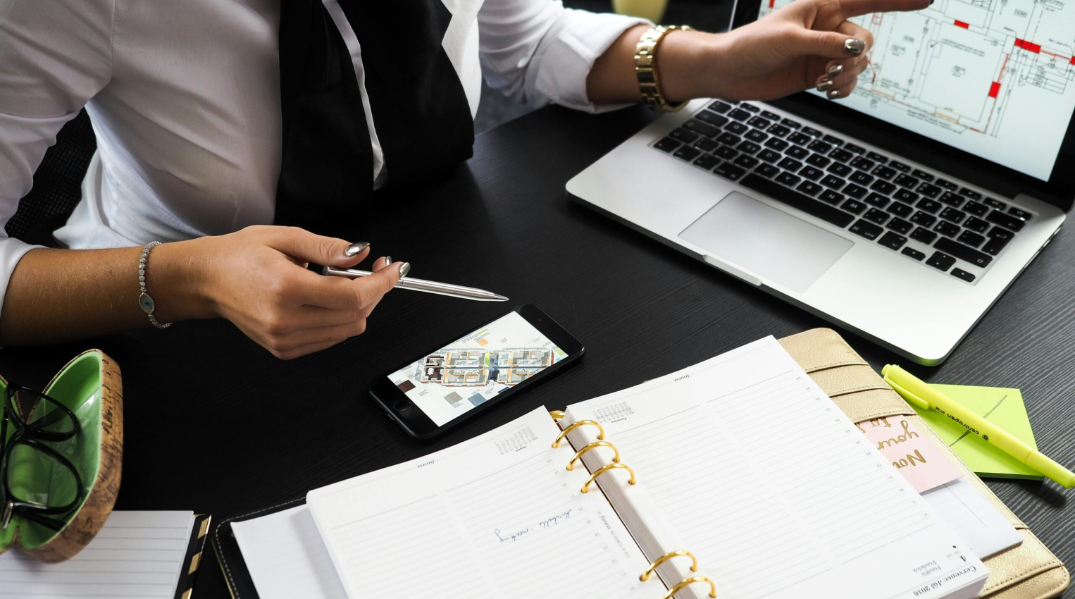 A business professional working on real estate project plans using multiple devices in an office setting.